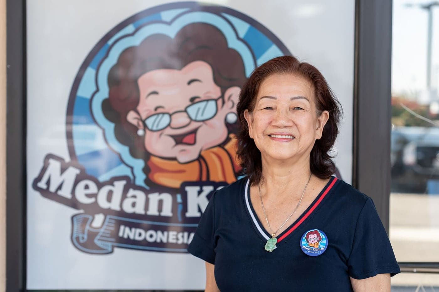 Siu Chen standing outside Medan Kitchen, by the window decal of the shop's logo