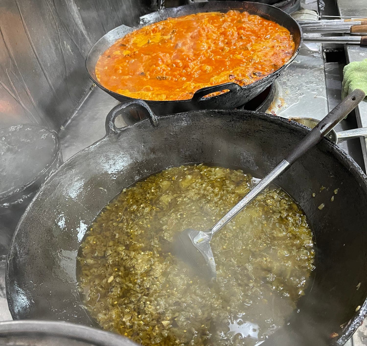 Two wide woks side by side, Sambal Hijau in one and Beef Rendang in the other, steam coming off both