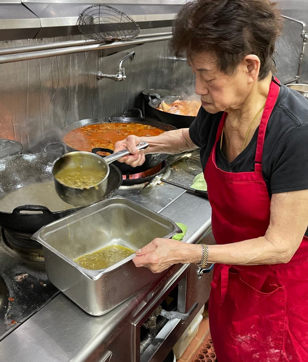 Siu Chen at the range, lifting a full pan of sayur with both hands